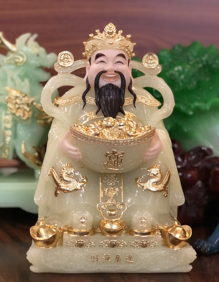 Thần Tiền ngồi trên những thỏi vàng lấp lánh, tay ôm thỏi vàng lớn tượng trưng cho giàu sang phú quý